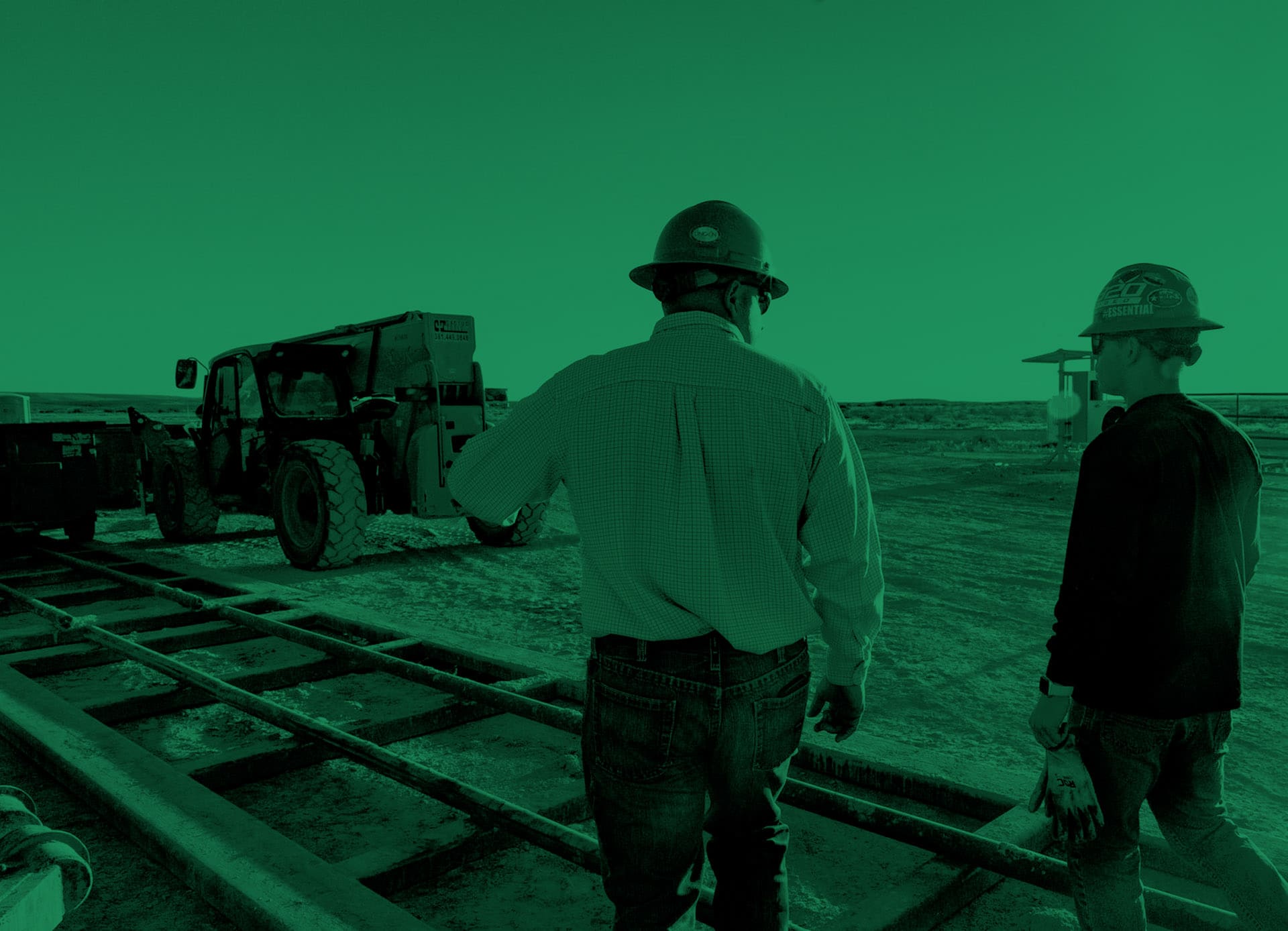 Two professionals from Tornado Production Services, viewed from behind, walk towards operational equipment at a well pad site. One carries gloves, indicative of their readiness for hands-on work in drill-out and clean-out operations, against the backdrop of a clear blue sky at dawn.