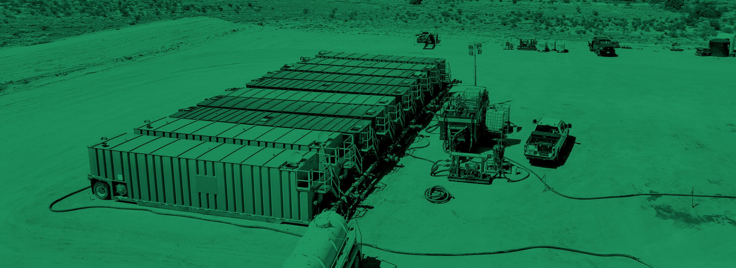 Two professionals from Tornado Production Services, viewed from behind, walk towards operational equipment at a well pad site. One carries gloves, indicative of their readiness for hands-on work in drill-out and clean-out operations, against the backdrop of a clear blue sky at dawn.